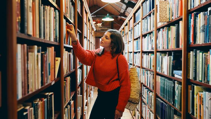 A person wearing a red jumper browsing books in a book shop in Hay-on-Wye